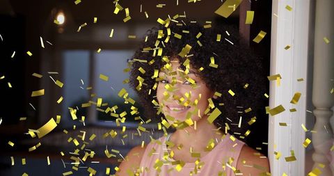 Sunlit woman celebrating with gold confetti at home doorway joyful lifestyle portrait