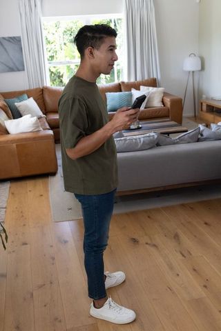African american man using handheld device in modern living room, relaxed lifestyle