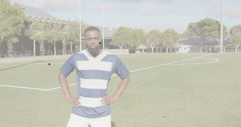 Standing athlete placing hands on hips on sports field wearing navy-white striped jersey