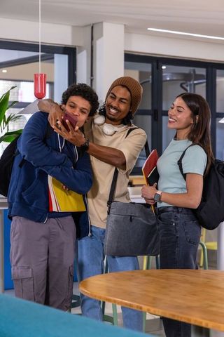 Multiracial college students sharing smartphone and notebooks in modern campus lounge