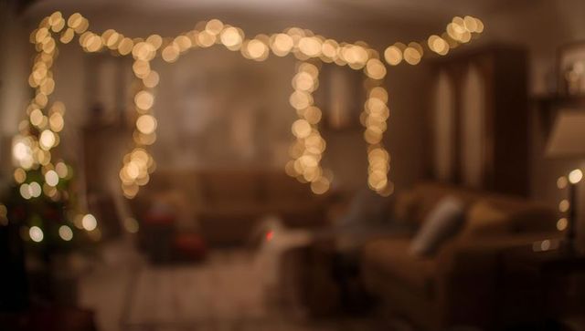 Warm string lights creating golden bokeh over cozy living room with holiday tree