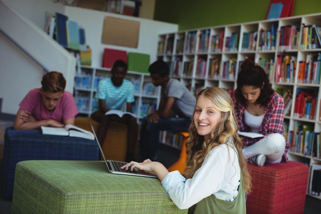 Group of teenagers studying in a school library. One student is smiling while using a laptop, surrounded by bookshelves and peers reading. Ideal for educational content, school promotions, and learning resources.
