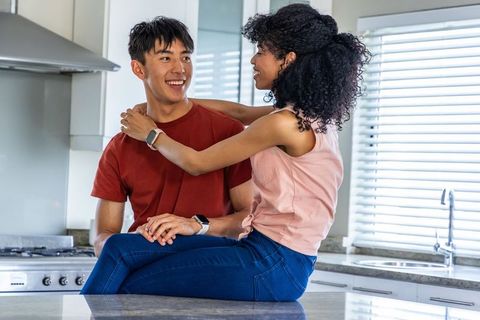 Smiling mixed-race couple embracing on modern kitchen countertop wearing smartwatches