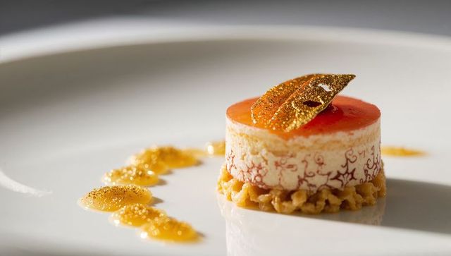 Refined citrus mousse entremet with edible gold leaf and praline crumble on white plate