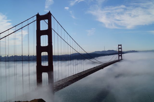 Golden Gate Bridge extends through thick morning fog creating a mystical and dramatic scenery. Ideal for use in travel and tourism materials, promotional content for San Francisco, architectural prints, and landscape photography collections.