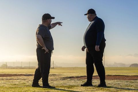 Coaching and mentoring on dawn sports field, two men pointing and planning training