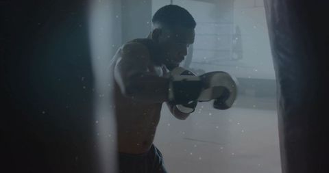 Muscular boxer training on heavy bag under dramatic gym lighting, intense focus