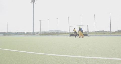 Field hockey attacker charging toward goal with goalkeeper blocking in bright yellow kit
