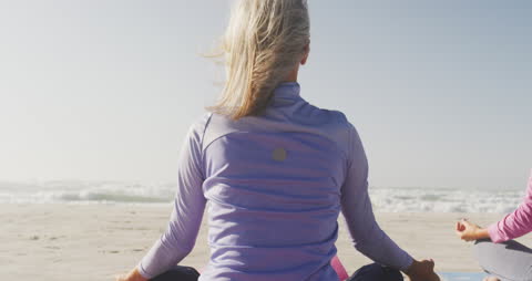 Senior Woman Meditating on Sunny Beach in Tranquility