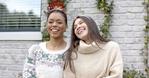 Diverse friends laughing outdoors wearing merry christmas headbands and cozy sweaters