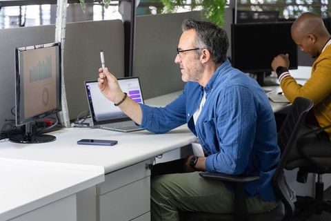 Middle-aged professional holding pen pointing at monitor in modern open office