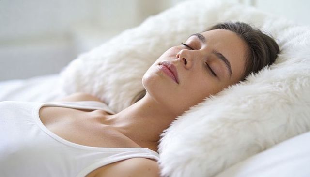 Serene young woman resting on fluffy white pillow, relaxing in bed for wellness and sleep