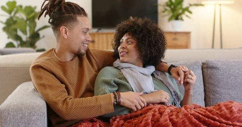 Cuddling diverse couple relaxing on sofa under cozy throw sharing warm intimate home moment