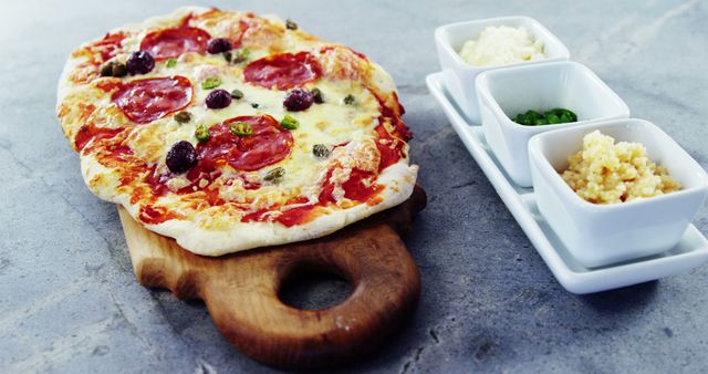 Fresh pepperoni pizza on a wooden board with side toppings including grated cheese, olives, and green peppers. Perfect for illustrating Italian cuisine, restaurant menus, or food blog posts about homemade pizza recipes.