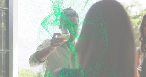 Bearded man raising glass through sunlit patio door with green digital mesh overlay