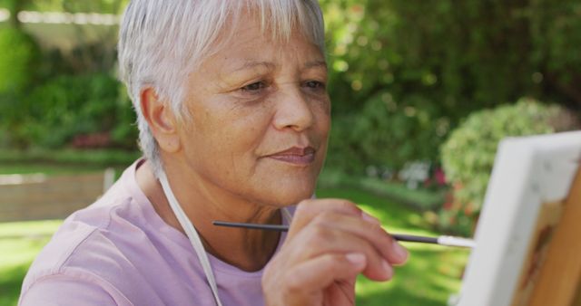 Image of happy biracial senior woman painting in garden. active retirement lifestyle, hobby and spending time outdoors.