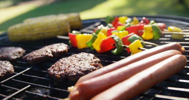 A variety of foods including hamburgers, hot dogs, corn on the cob, and skewered vegetables are being grilled outdoors. Grilling is a popular cooking method for outdoor gatherings and emphasizes the enjoyment of preparing and eating food in a casual, social environment.