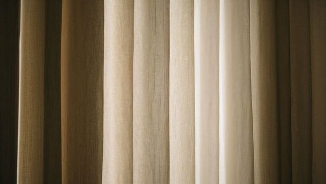 Layered beige curtains casting soft vertical shadows with sheer linen panel