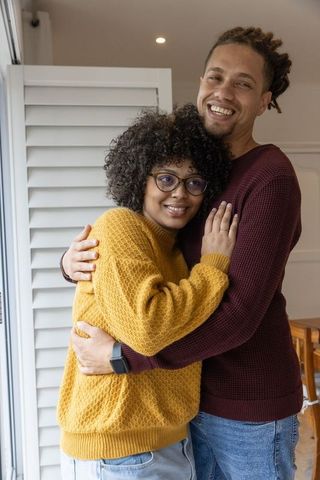 Couple hugging at home showing engagement ring, cozy sweaters and warm intimate moment