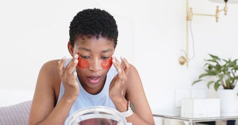 Applying red hydrogel eye patches during morning skincare routine at minimalist vanity