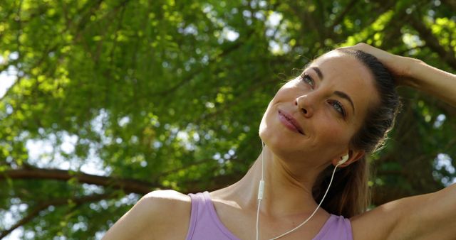 Runner stretching neck listening to music in the park on a sunny day