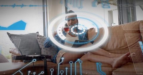 Relaxing woman using tablet while sipping tea with augmented reality interface on couch