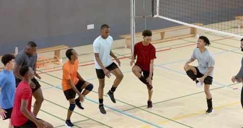 Diverse male volleyball team warming up on indoor court before practice