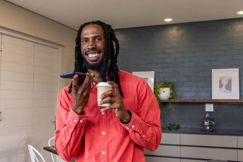 African american man talking on smartphone while holding coffee in modern breakroom