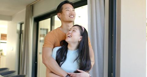 Young asian couple embracing and smiling by modern minimalist apartment sliding door
