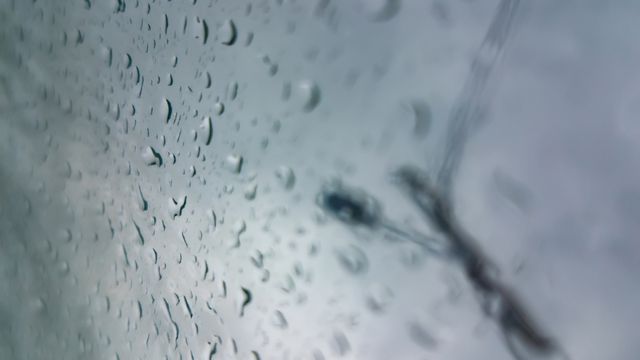 Raindrops on blurred windshield creating an abstract view during a storm. Ideal for concepts like weather, driving conditions, safety, or abstract backgrounds. Can be used in articles, blogs, presentations, and weather forecasting materials.