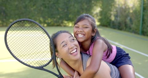 Joyful Mother and Daughter Piggybacking on Tennis Court