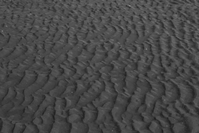 Close-up of black sand dunes showing intricate patterns and textures in monochrome. Useful for backgrounds, wallpapers, abstract art, and nature-related themes. Suitable for environmental concepts and minimalist designs.