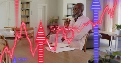 Senior man reviewing finances at home with laptop, paperwork and rising stock charts