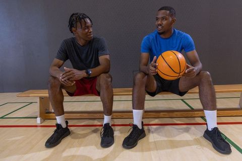 African american men sitting on bench holding basketball talking in gymnasium