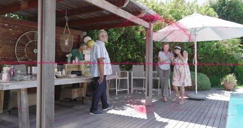 Adults mingling poolside backyard party under wooden pergola by swimming pool