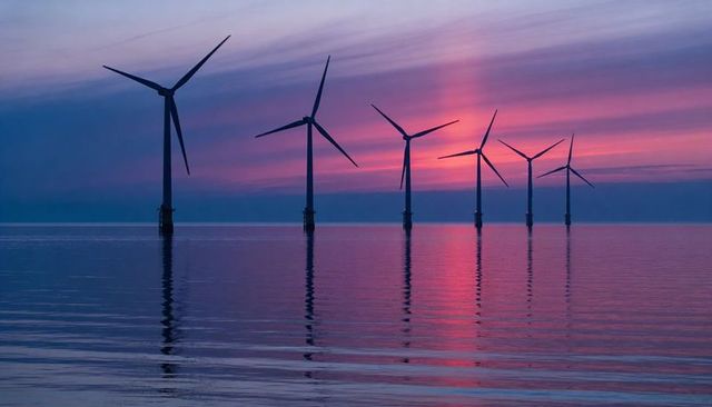 Offshore wind turbines standing in row reflecting pink purple twilight over calm sea