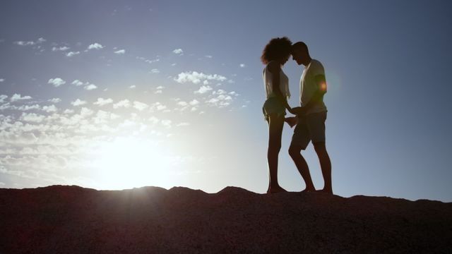 This scene captures a loving couple standing on a beach rock against a mesmerizing sunset skyline. The way they hold hands exemplifies affection and serenity amid nature. Useful for advertisements about romance, travel, and lifestyle inspirations or as part of storytelling for beach-oriented getaways.