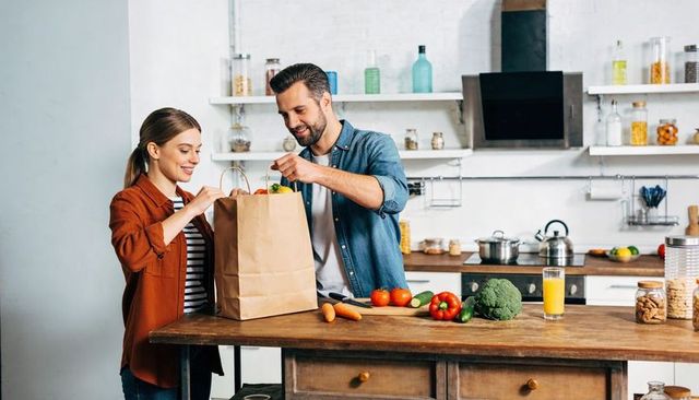 Couple unpacking groceries and preparing fresh vegetables on rustic kitchen island