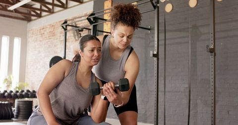 Female trainer spotting client during dumbbell curl in urban gym, strength coaching moment