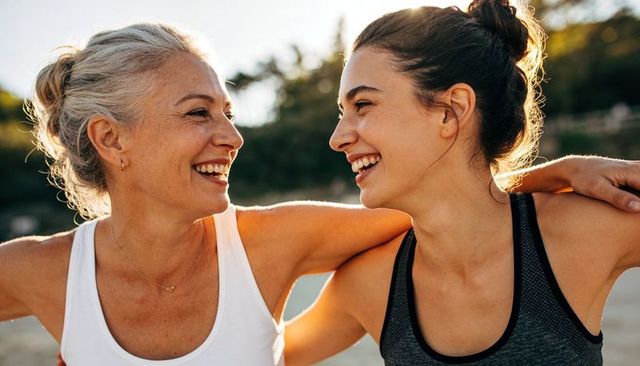 Intergenerational friends laughing embracing on sunlit beach during golden hour