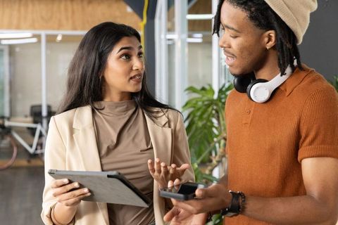 South asian woman and black man collaborating with tablet and smartphone in modern office