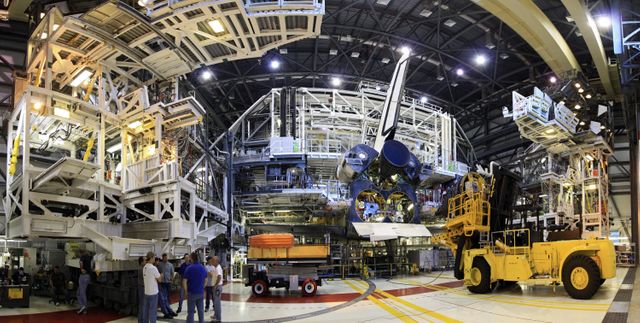 Space shuttle Discovery is shown in the Orbiter Processing Facility-1 during transition activities. Engineers and technicians in the facility are working to install replica shuttle main engines on Discovery. This photo captures the complexity of the assembly and engineering efforts. It could be used for educational content, articles about NASA's shuttle program, or discussions about space shuttle retirement and display preparation.