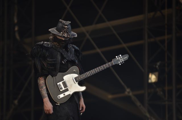 Musician in elaborate costume playing electric guitar during live stage performance. Suitable for use in advertisements for music festivals, live concerts, rock music promotions, and theatrical productions. Perfect for editorial use in music magazines and websites focusing on artist features and concert highlights.