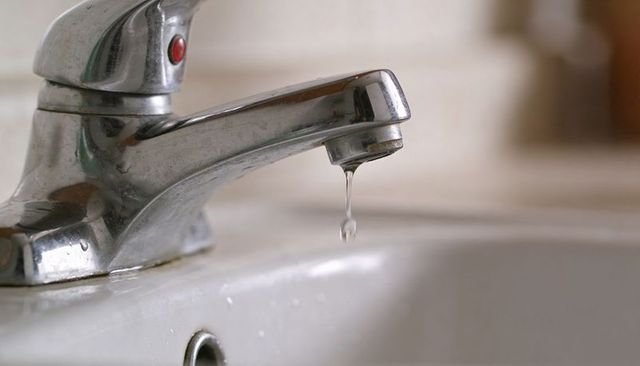 Dripping chrome faucet forming water droplet with limescale spots on bathroom sink