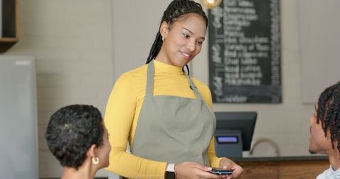 Friendly barista serving customers using handheld card reader at cozy cafe counter