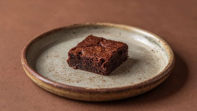 Chocolate brownie square on rustic speckled plate with cocoa crumbs minimalist food