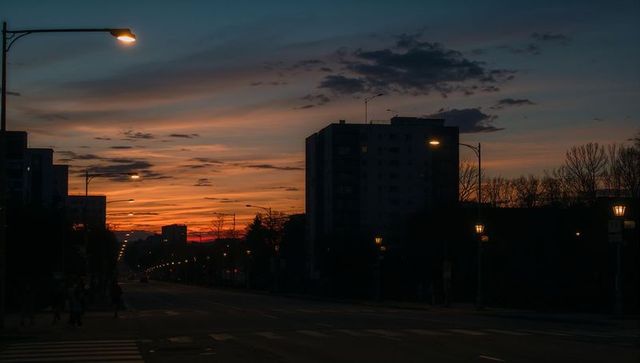 Midrise silhouette against dramatic sunset on urban avenue with glowing streetlights