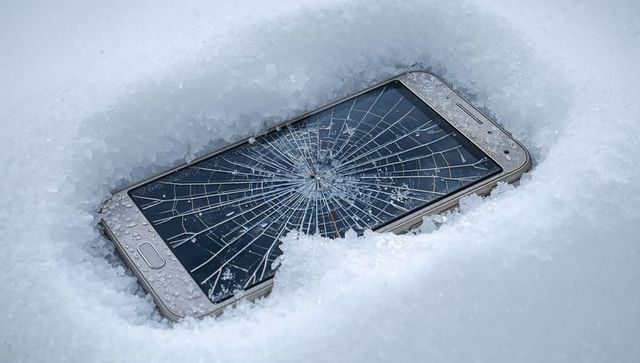 Cracked smartphone screen buried in snow with ice droplets showing winter damage