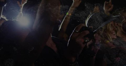 Attendee recording live concert with smartphone flash, rings and energetic crowd