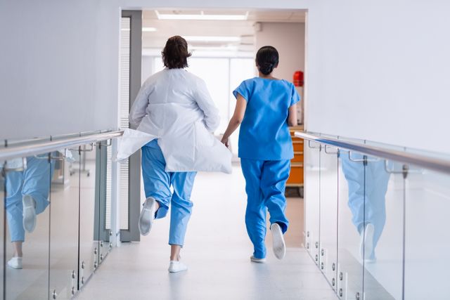 Nurse and doctor running through hospital corridor, indicating urgency and emergency response. Useful for illustrating healthcare, medical emergencies, teamwork in medical settings, and the dedication of medical professionals.